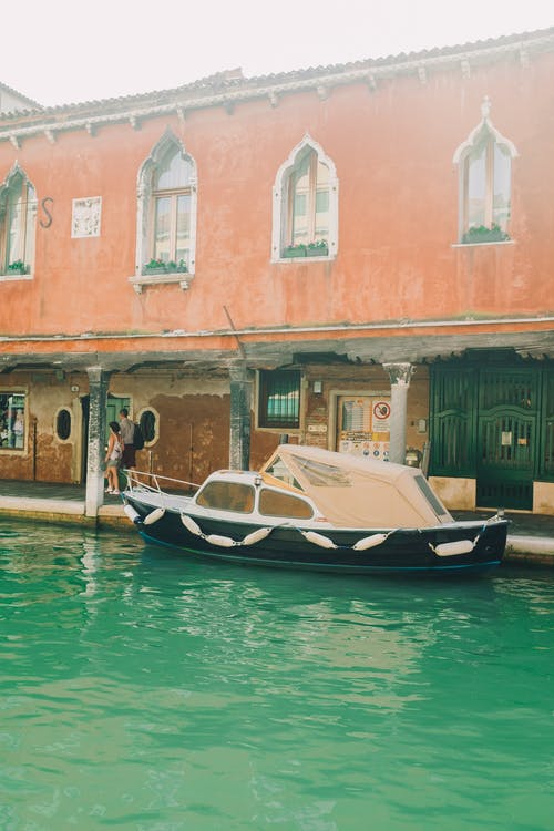 棕色和白色的小船在布朗混凝土建筑附近的水面上 · 免费素材图片