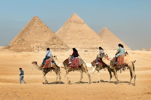 四人骑着骆驼穿越金字塔 · 免费素材图片