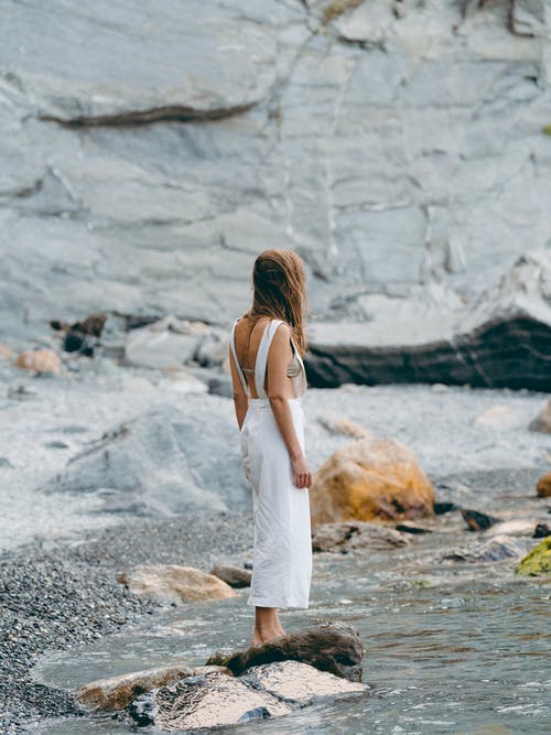 白色背心裙站在水体附近的岩石上的女人 · 免费素材图片