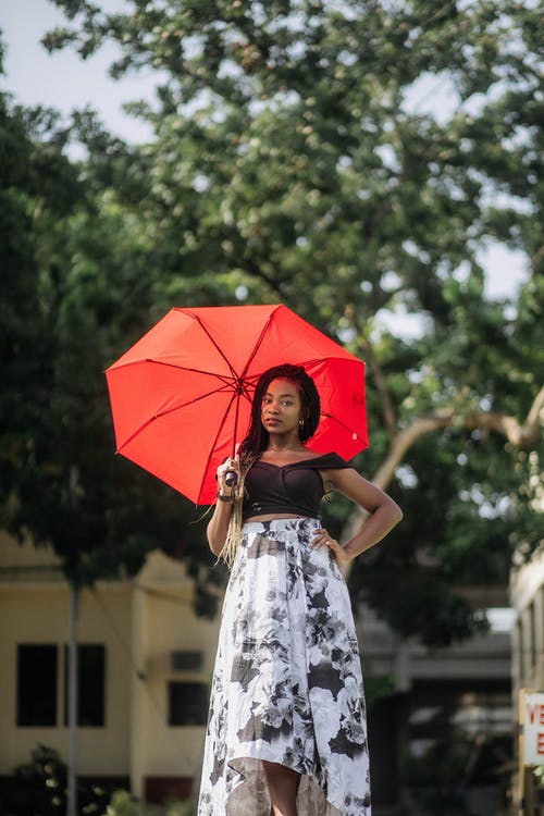 女人穿着黑色作物顶部和白色和黑色的花裙子时，拿着红色的伞 · 免费素材图片