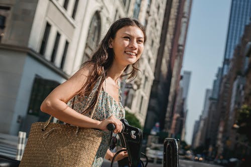 快乐的年轻族裔女子骑着自行车在摩天大楼附近的现代城市 · 免费素材图片