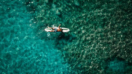 漂浮在海上躺在冲浪板上的匿名男运动员 · 免费素材图片