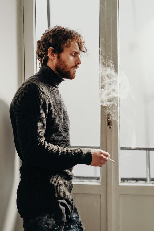 站在白色的木门吸烟旁边的黑色毛衣的男人的侧视图照片 · 免费素材图片