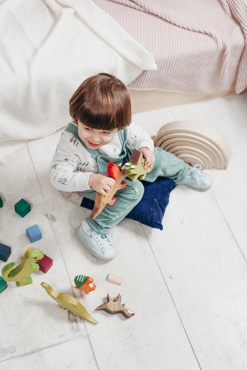 白色的长袖上衣和蓝绿色的粗蓝布长裤玩玩具的孩子 · 免费素材图片