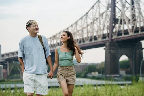 幸福的民族情侣在桥边的公园里漫步时手牵着手 · 免费素材图片