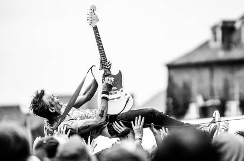 拿着stratocaster吉他的人举起的人的灰度照片 · 免费素材图片