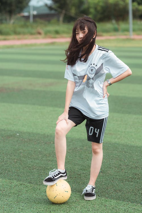 女人站在足球场上穿白色足球服衬衫和黑色短裤 · 免费素材图片