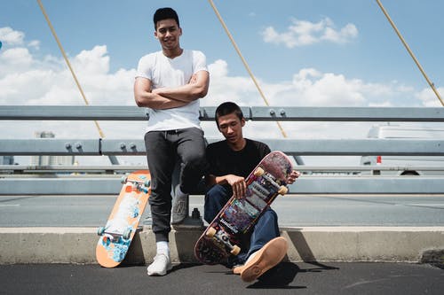 微笑与桥路面上的滑板的族裔男性伙伴 · 免费素材图片