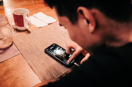 木制的桌子上的男人抚摸智能手机 · 免费素材图片