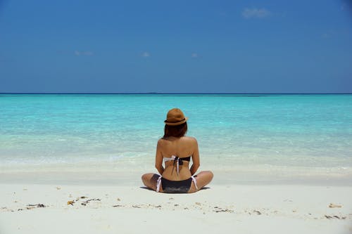 女人穿着黑色和白色的胸罩，坐在白色的沙滩上 · 免费素材图片