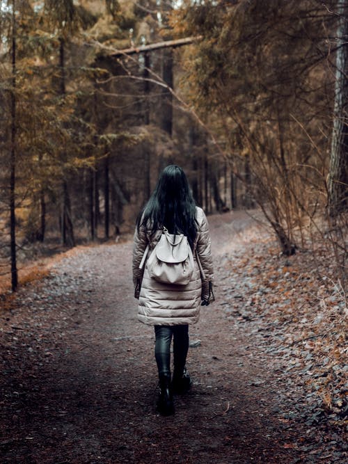 女人背着背包走在树木被包围的通路上 · 免费素材图片