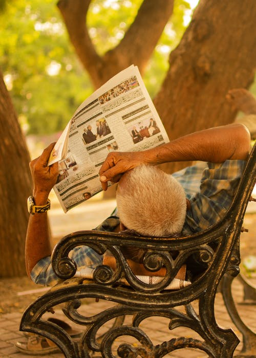 躺在黑金属长凳上的人阅读报纸 · 免费素材图片