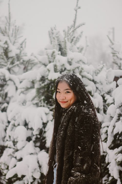女人穿着黑色的冬天站在冰雪覆盖的树木附近 · 免费素材图片