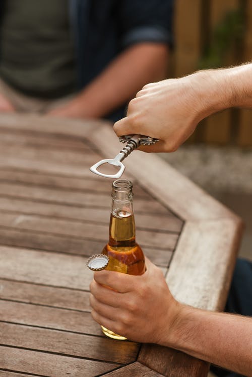 男人用开瓶器打开玻璃瓶啤酒 · 免费素材图片