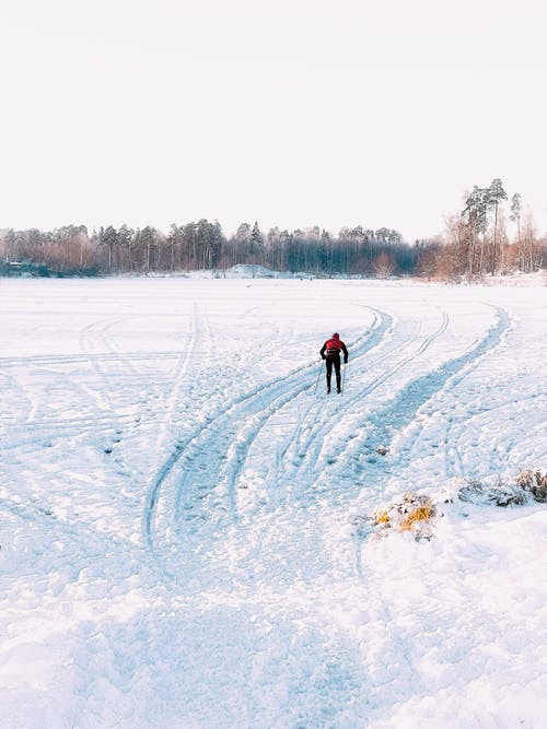 红色外套和蓝色裤子的人在积雪的地面上行走 · 免费素材图片