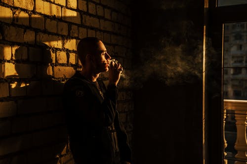男子吸烟和倚在砖墙上 · 免费素材图片