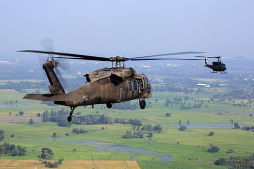 白天在绿色的田野上空飞行的棕色直升机 · 免费素材图片