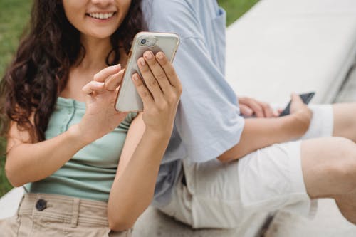裁剪微笑的女人在男朋友附近的智能手机上冲浪互联网 · 免费素材图片