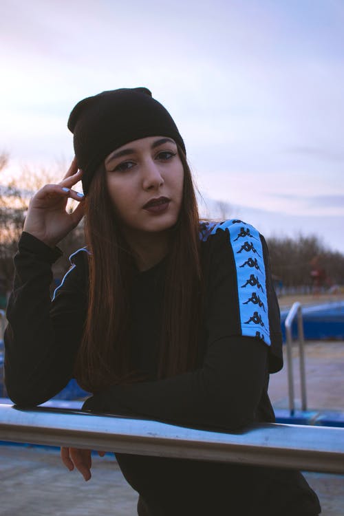 靠在金属栏杆上的黑色上衣和黑色编织帽的女人 · 免费素材图片