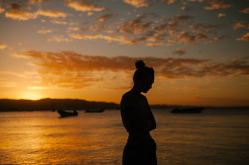 悲伤的女人站在海上海岸在日落时 · 免费素材图片