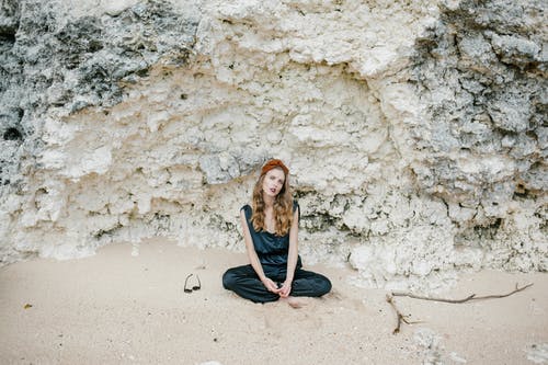 平静的女士坐在海滩上的岩石附近 · 免费素材图片
