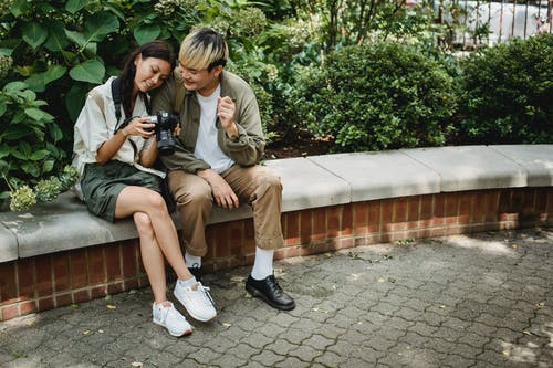 性格开朗的亚洲夫妇，坐在长椅上与相机拍照 · 免费素材图片