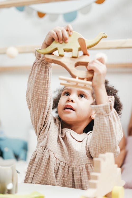 白色和棕色条纹连帽衫的女孩举起双手玩具 · 免费素材图片