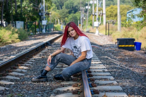 白色t恤和蓝色牛仔牛仔裤，坐在火车栏杆上的女人 · 免费素材图片
