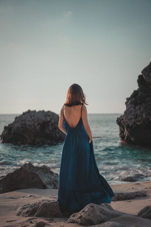不可识别的女性女人穿着长裙站在岩石的海边 · 免费素材图片