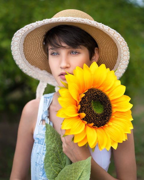 女人拿着向日葵戴黄色太阳帽 · 免费素材图片