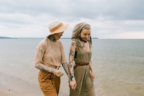 妇女在海滩上散步时手牵着手的照片 · 免费素材图片