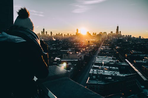 穿黑夹克的男子站在日落时建筑物的顶部 · 免费素材图片