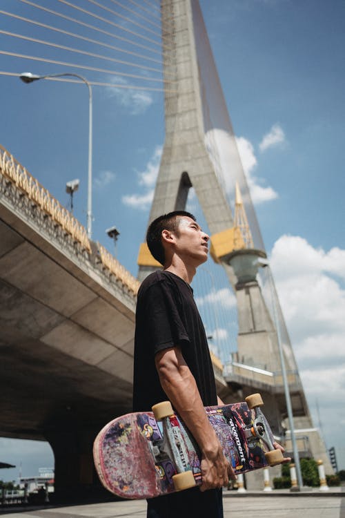 沉思的亚裔运动员，对城市桥梁的滑板 · 免费素材图片