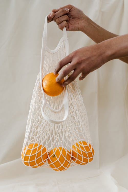 在白色网中持有橙色水果的人 · 免费素材图片