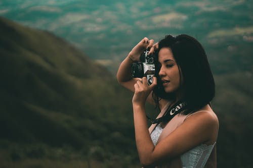 女人拿着一个黑色的数码单反相机和拍照 · 免费素材图片