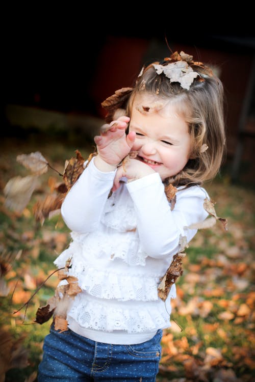 聚焦在白色的长袖衬衫，棕色的叶子，在她头上的女孩的照片 · 免费素材图片