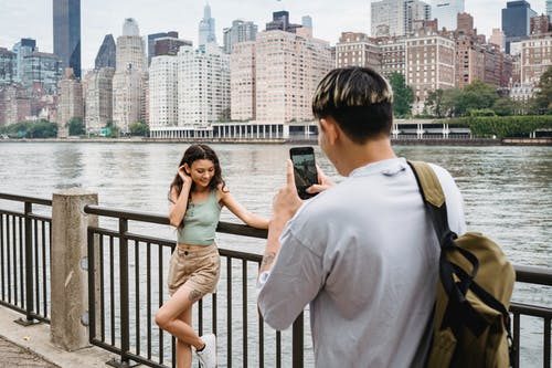 年轻人拍摄智能手机的女朋友在约会期间在河附近的城市市区 · 免费素材图片