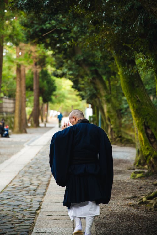 在杂草丛生的树木之间的人行道上漫步的匿名亚洲牧师 · 免费素材图片