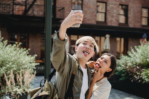 快乐年轻的民族夫妇在智能手机上拍照时制作有趣的鬼脸 · 免费素材图片