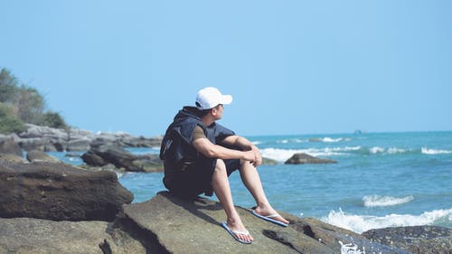 男子坐在海边的岩石上 · 免费素材图片