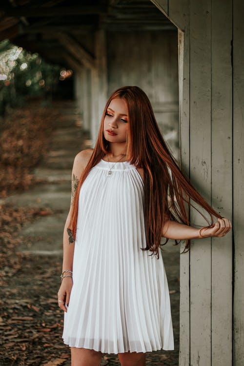 站在灰色的木墙上的白色无袖连衣裙的女人 · 免费素材图片
