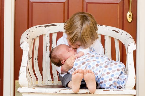 男孩抱着和亲吻婴儿坐在椅子上 · 免费素材图片