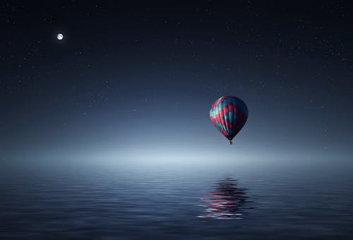 红色和蓝色的热气球在夜间漂浮在水面上的空气 · 免费素材图片