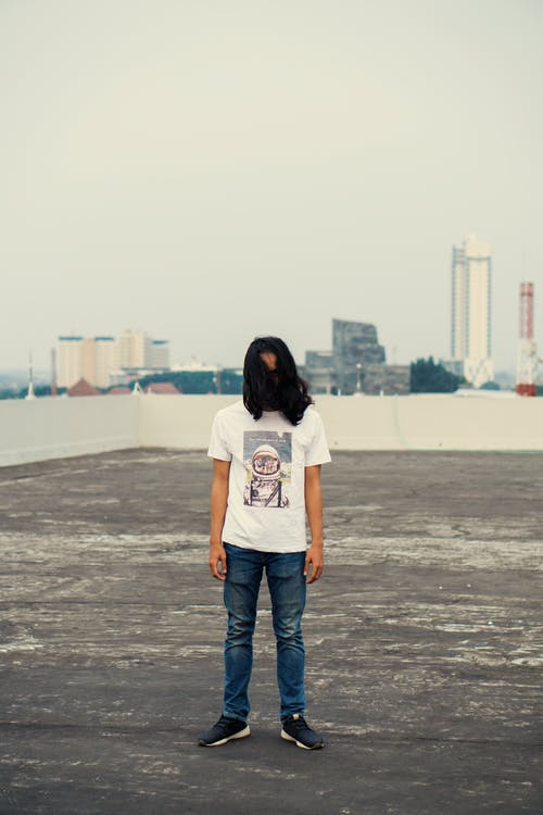 白色t恤和蓝色牛仔牛仔裤，站在灰色的沙滩上的女人 · 免费素材图片