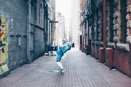 在巷子里踢足球的蓝夹克和蓝色牛仔牛仔裤的男人 · 免费素材图片