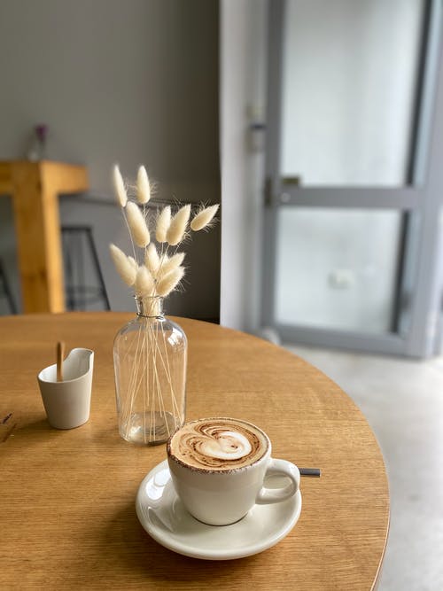 在桌子上花瓶旁边的茶碟上的白色陶瓷杯 · 免费素材图片