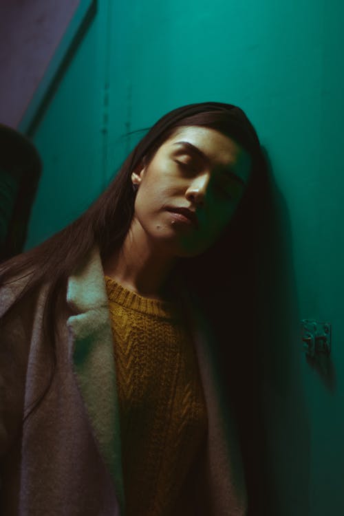 女人穿着白色粉红色外套倚在蓝色的墙上 · 免费素材图片