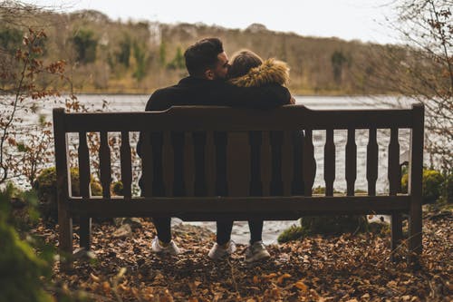 男人坐在水体前的长椅上亲吻女人的头 · 免费素材图片