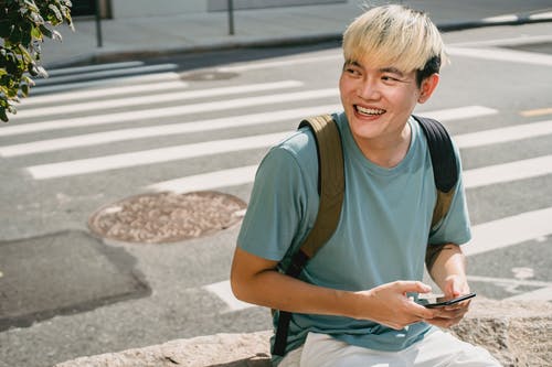 亚洲年轻人微笑和使用智能手机 · 免费素材图片