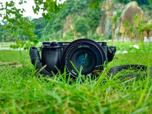 黑色的索尼单反相机在棕色和绿色的山前的绿色草地上 · 免费素材图片